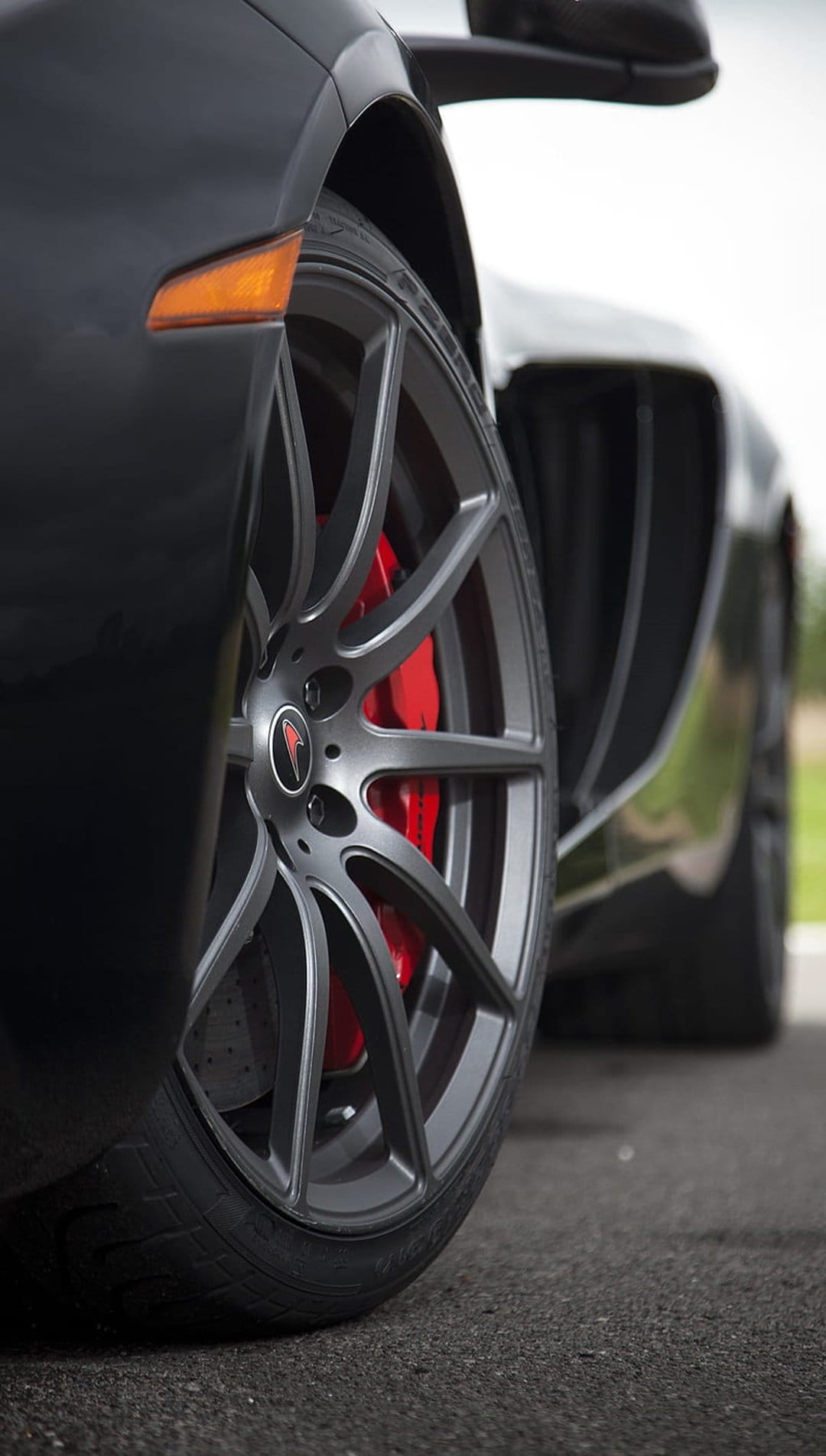 Matte grey multi-spoke wheel rim revealing bright red brake calipers on a dark performance car outdoors.