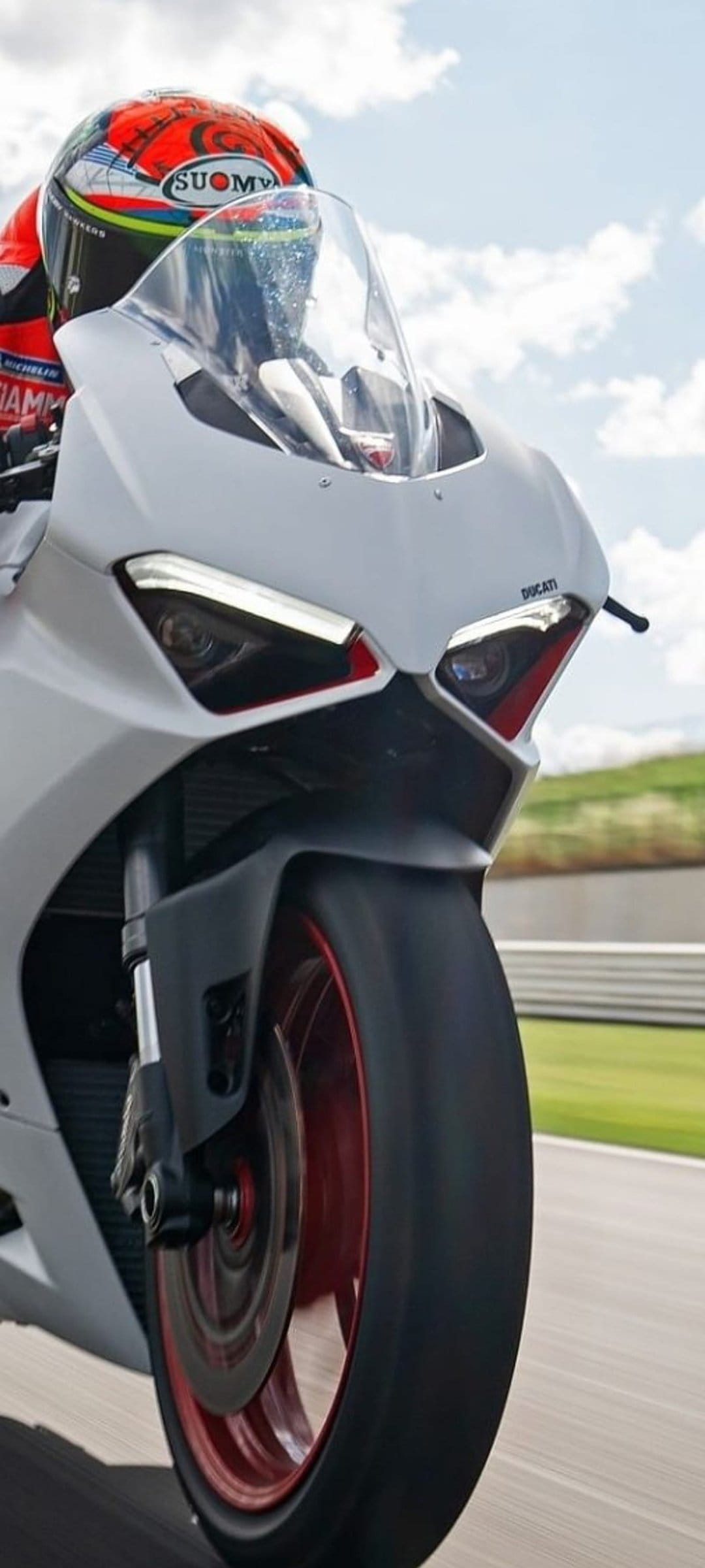 Ducati motorcycle rider leans into a track corner wearing a Suomy helmet and professional white racing leathers.