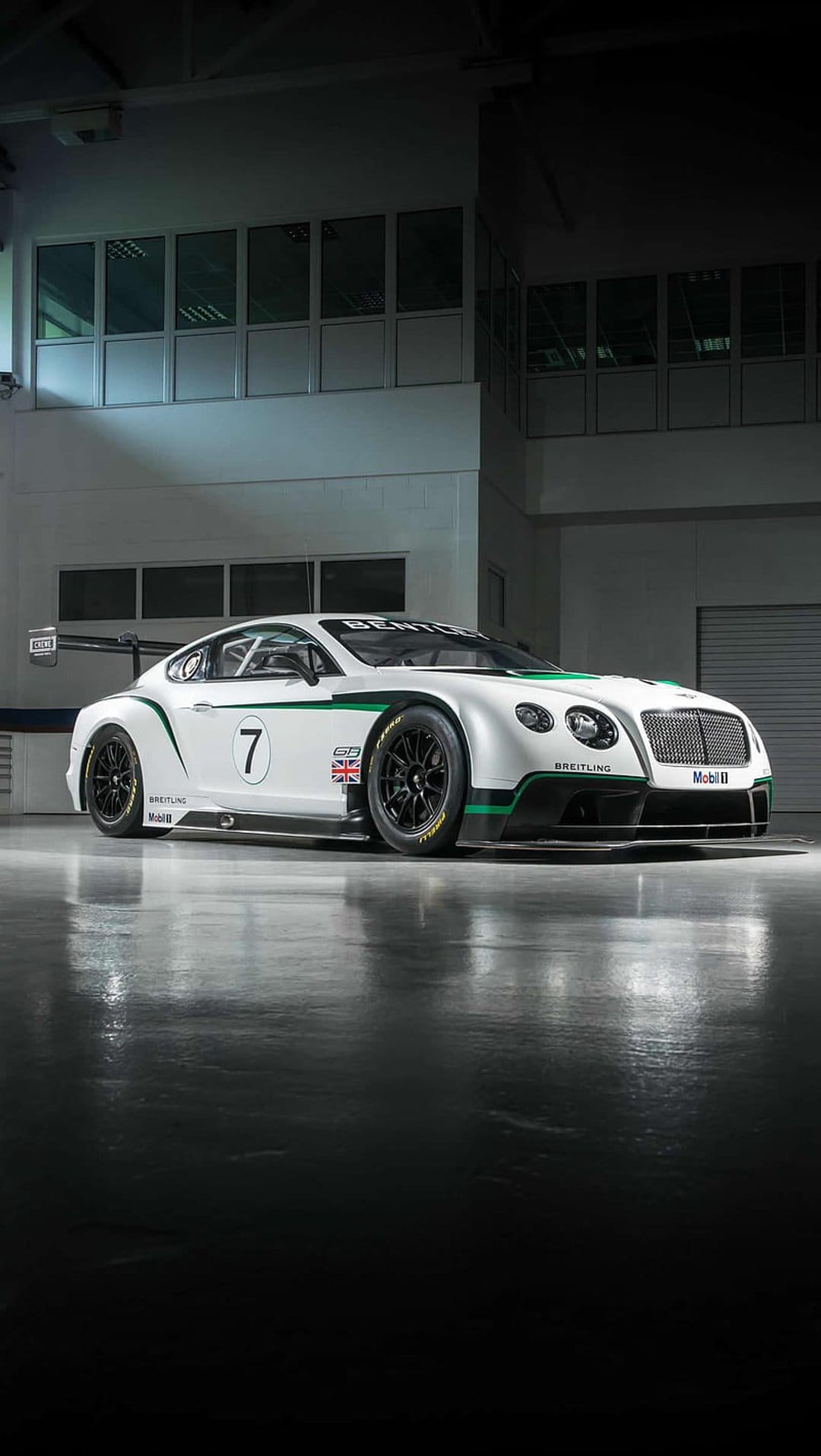 Bentley Continental GT3 race car with white and green livery parked on a reflective floor in a bright pit lane.