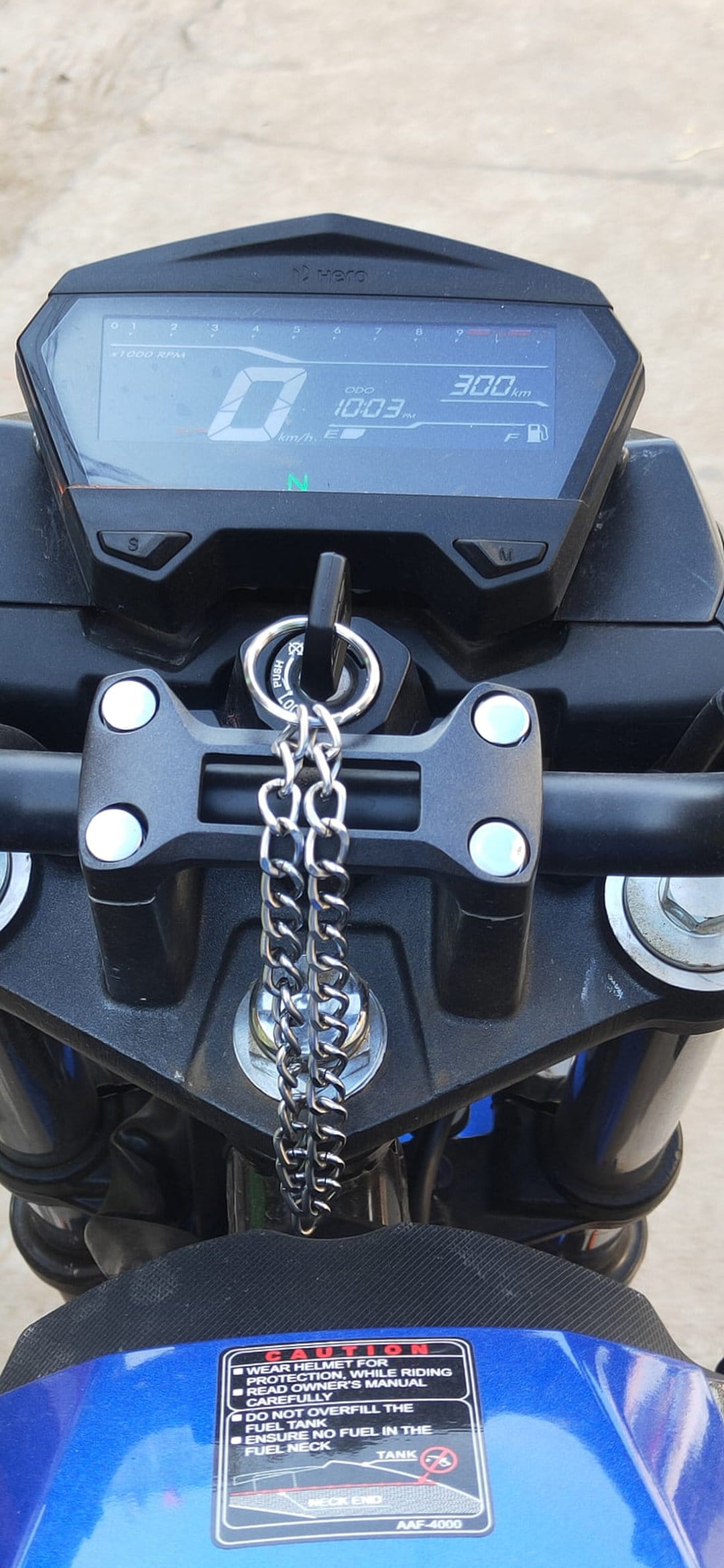 Motorcycle handlebars with a digital speedometer, ignition key on a silver chain, and blue painted bodywork.