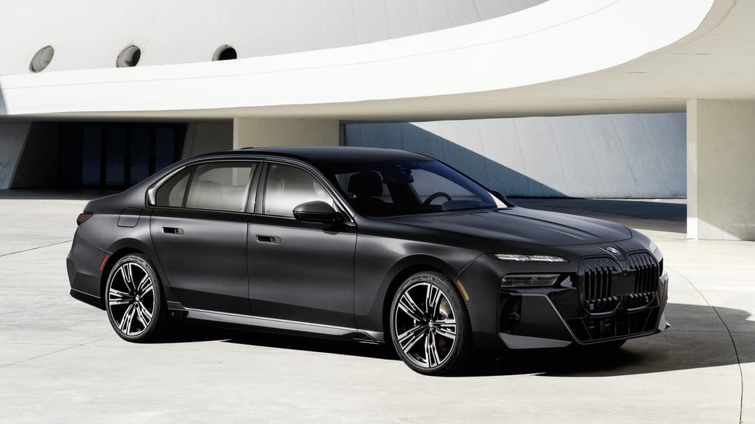 Matte black BMW luxury sedan parked in front of a curved white concrete building in daylight.