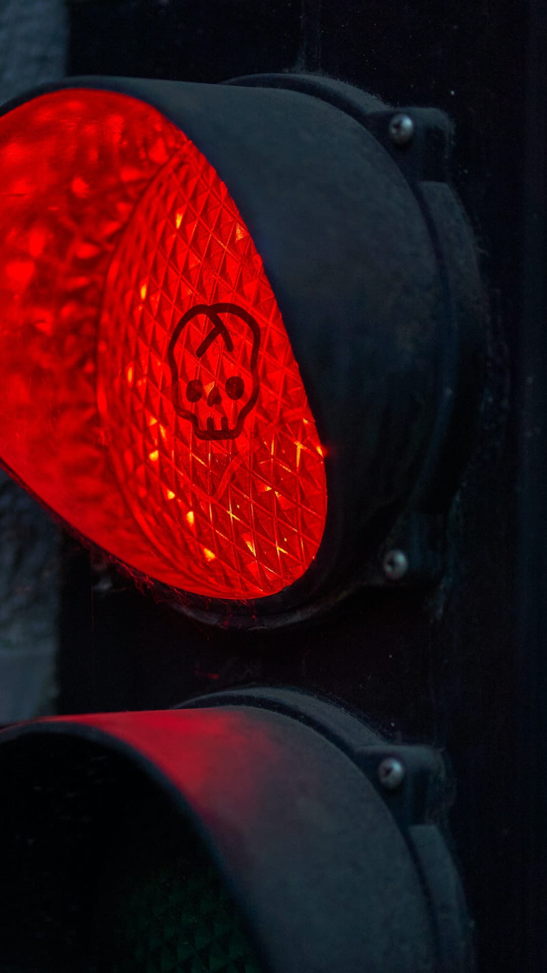Red skull symbol glowing on a textured traffic light lens surrounded by a dark metal housing and deep shadows.