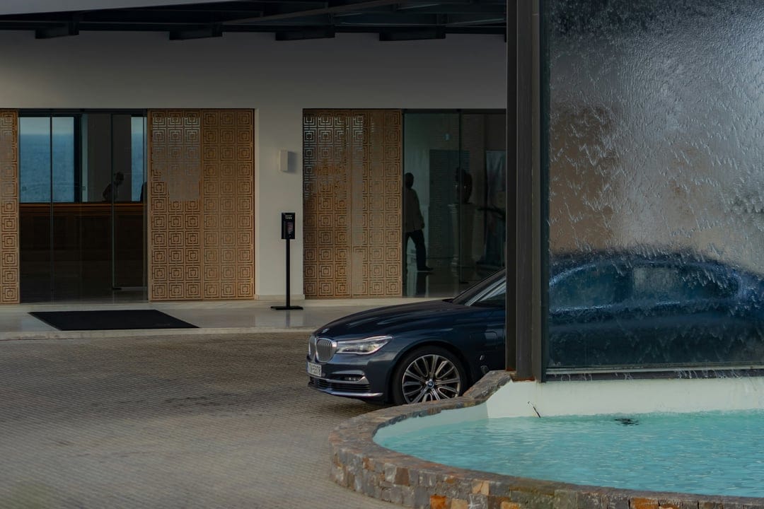 Dark blue BMW sedan parked at a luxury hotel entrance with a glass waterfall feature and wooden screen panels.