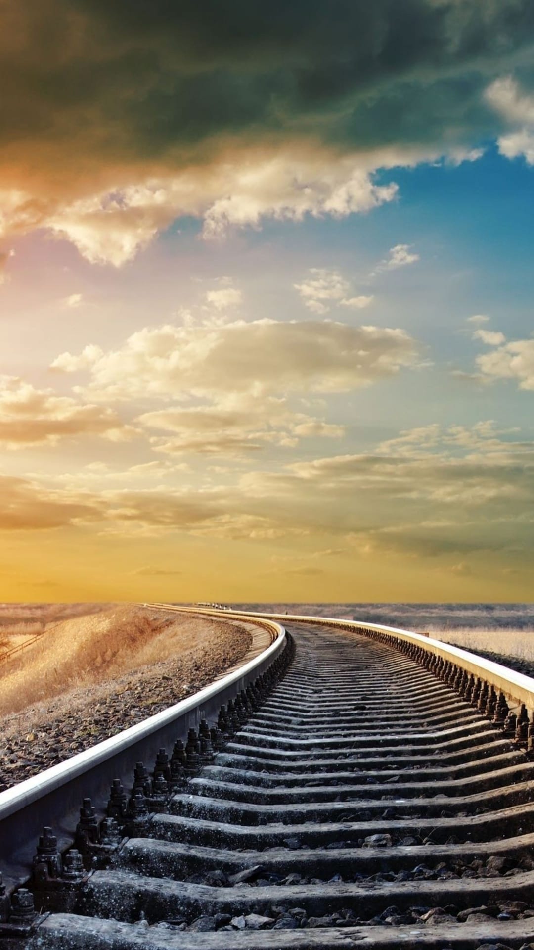 Railway tracks receding toward a distant horizon under a dramatic blue and golden sky with swirling clouds.