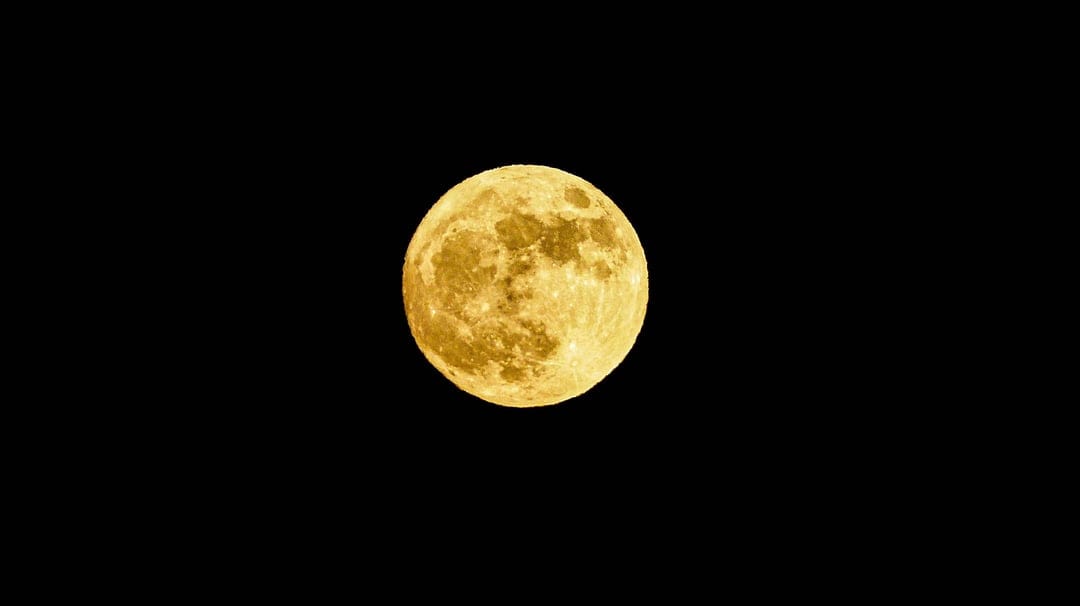 Full amber moon with detailed craters and maria centered against a deep black, starless nocturnal sky.