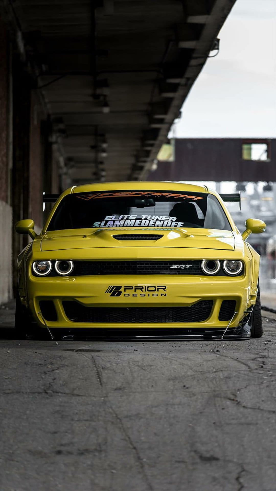 Yellow Dodge Challenger SRT Hellcat with a widebody kit and custom decals shown from a low ground-level angle.