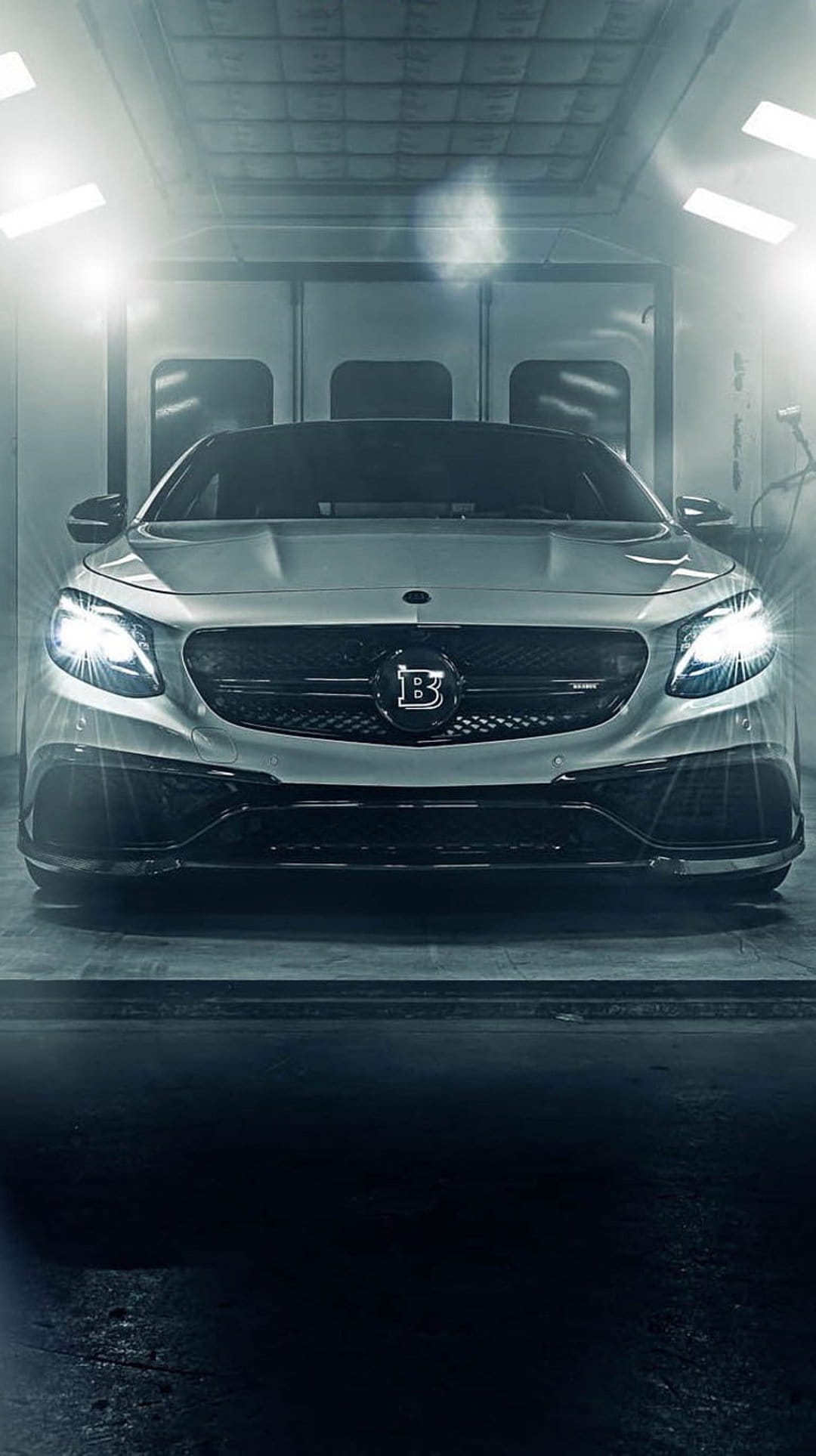 Brabus S-Class Coupe with glowing headlights and a B emblem stands in a professional lit paint booth.