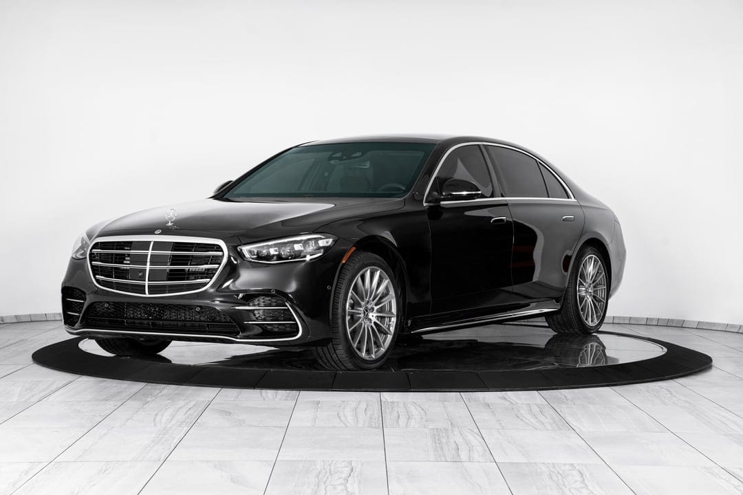 Black Mercedes-Benz S-Class sedan on a circular platform in a bright white studio with silver wheels.