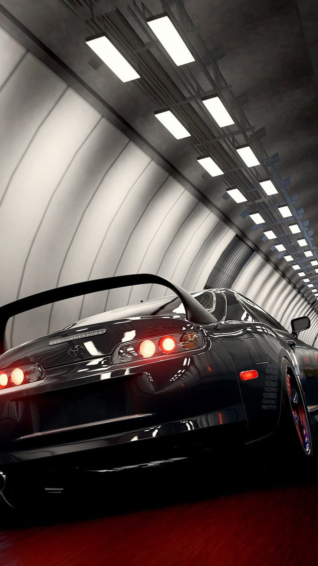 Black Toyota Supra with glowing red taillights racing through a bright modern tunnel on a wet road surface.