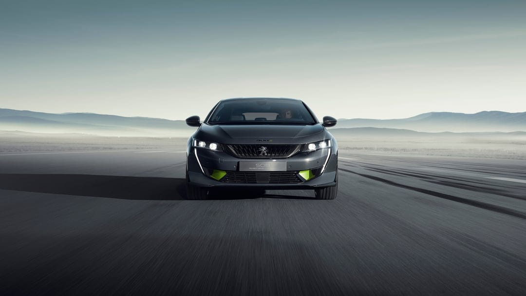 Dark grey Peugeot 508 sport sedan with lime green accents on a vast asphalt road against misty mountains.