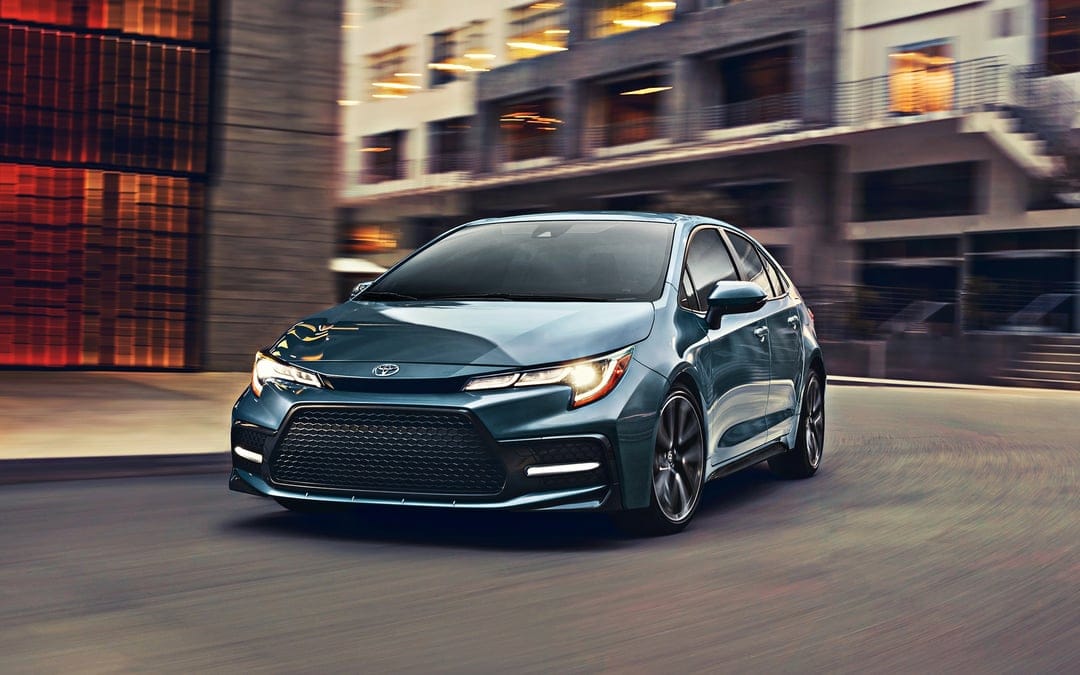 Blue modern sedan driving on a city street with motion blur and glowing headlights at twilight.