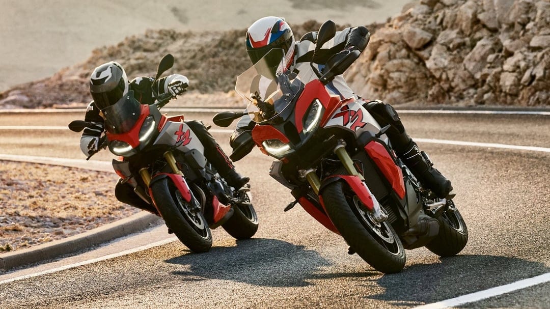 Two red and silver sport motorcycles leaning into a turn on a mountain highway during a warm golden hour sunset.