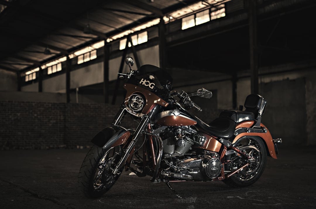Orange Harley Davidson motorcycle with chrome accents parked inside a dark, sunlit industrial warehouse.