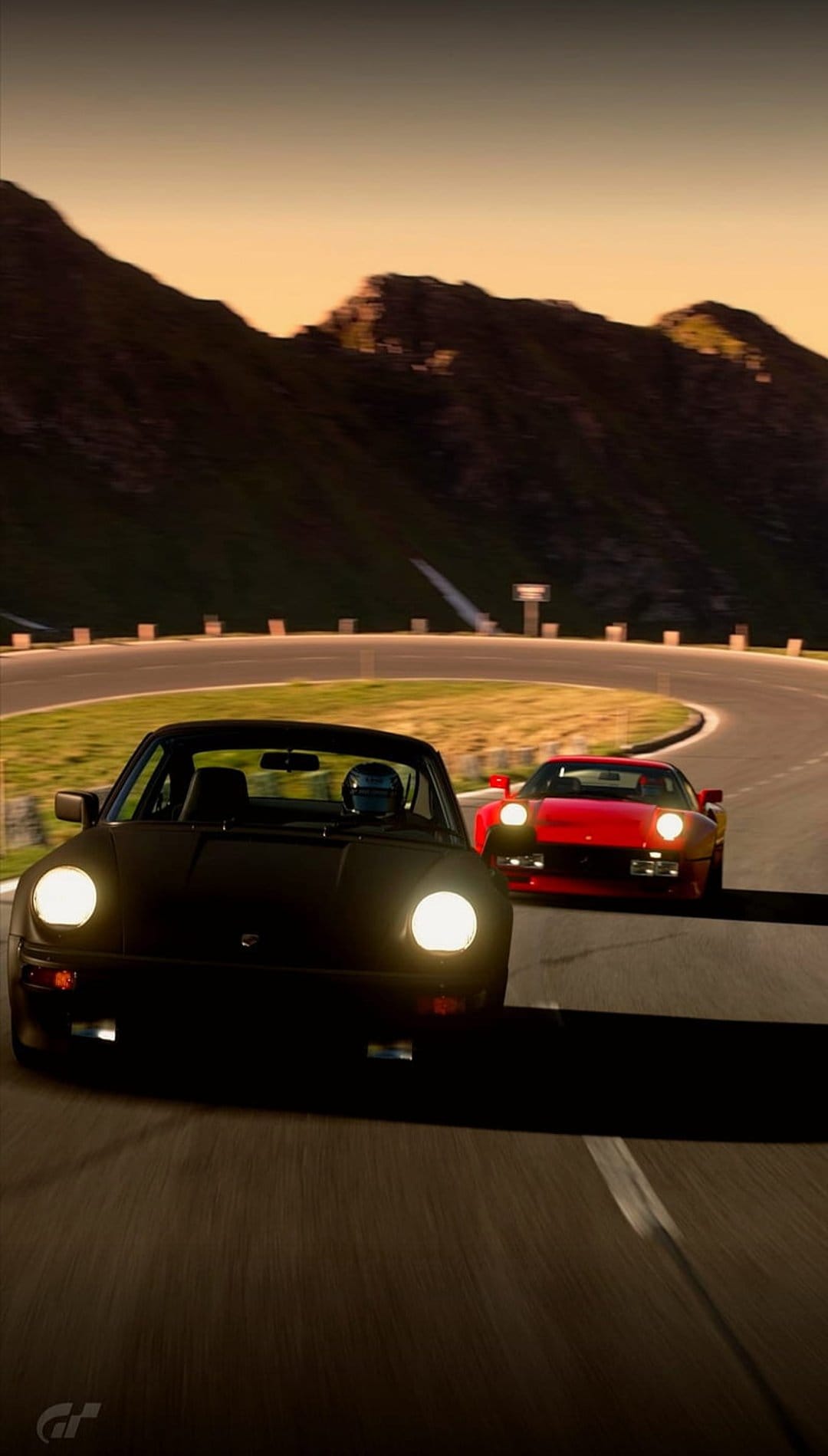 Black Porsche and red Ferrari navigate a winding mountain road during a vibrant golden hour alpine sunset.