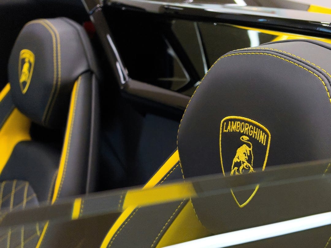 Lamborghini bucket seats in black leather with yellow contrast stitching and the brand shield logo on the headrest.