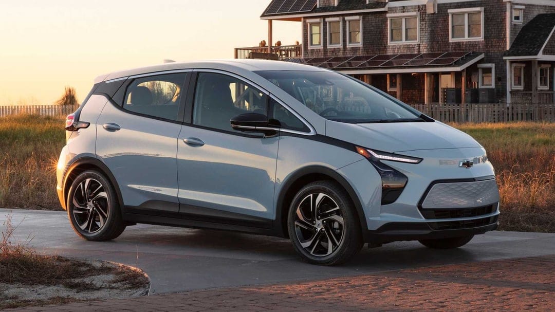 Chevrolet Bolt EV in Ice Blue Metallic parked on a driveway at sunset with a shingle house background.