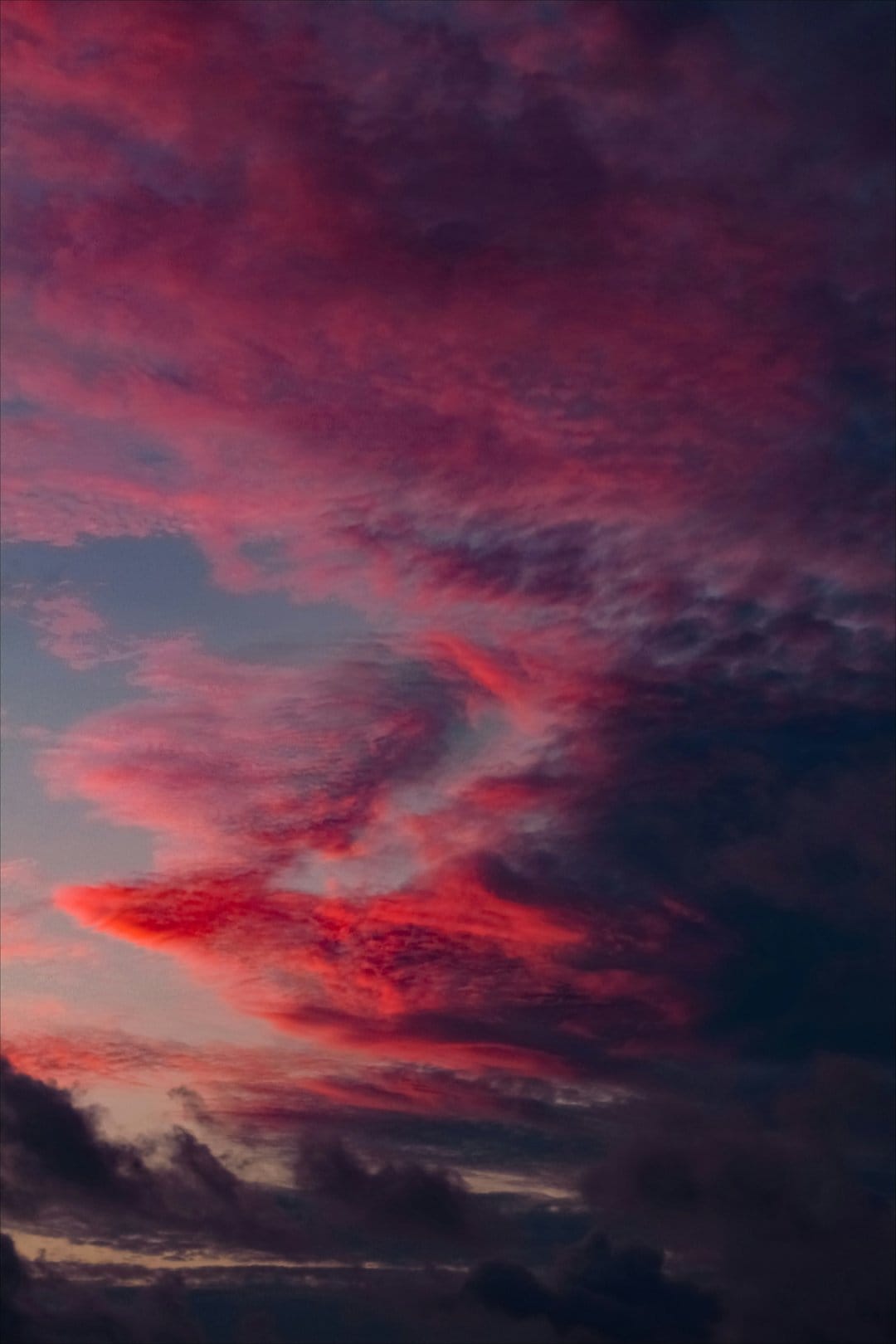 Swirling fuchsia and purple clouds blanket a twilight sky with soft edges and deep indigo shadows in the background.