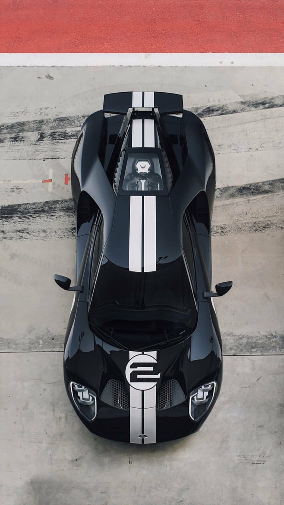 Black Ford GT race car with white stripes captured from above on a concrete track with red and white borders.