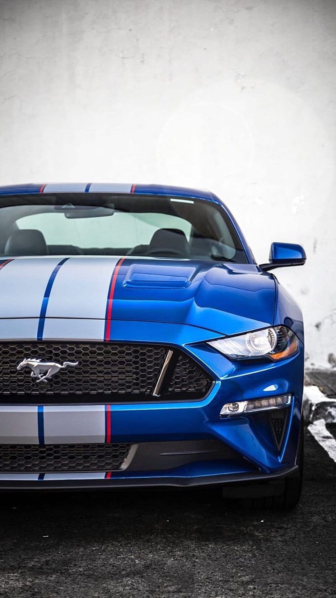 Blue Ford Mustang with red and silver stripes centered against a textured white wall in a vertical car portrait.