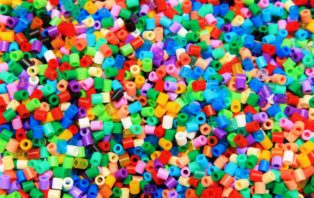 Multicolored cylindrical plastic fuse beads form a dense, textured pile in a vibrant top-down composition.