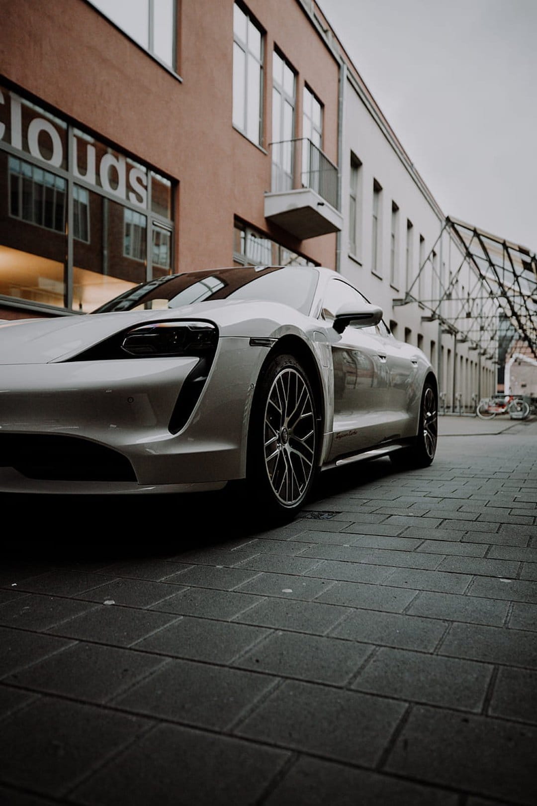 White luxury electric car parked on a textured cobblestone street by a glass building during golden hour.