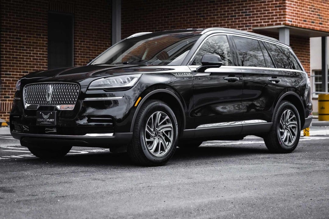 Black Lincoln Aviator SUV parked on asphalt with a brick building background and chrome accents.