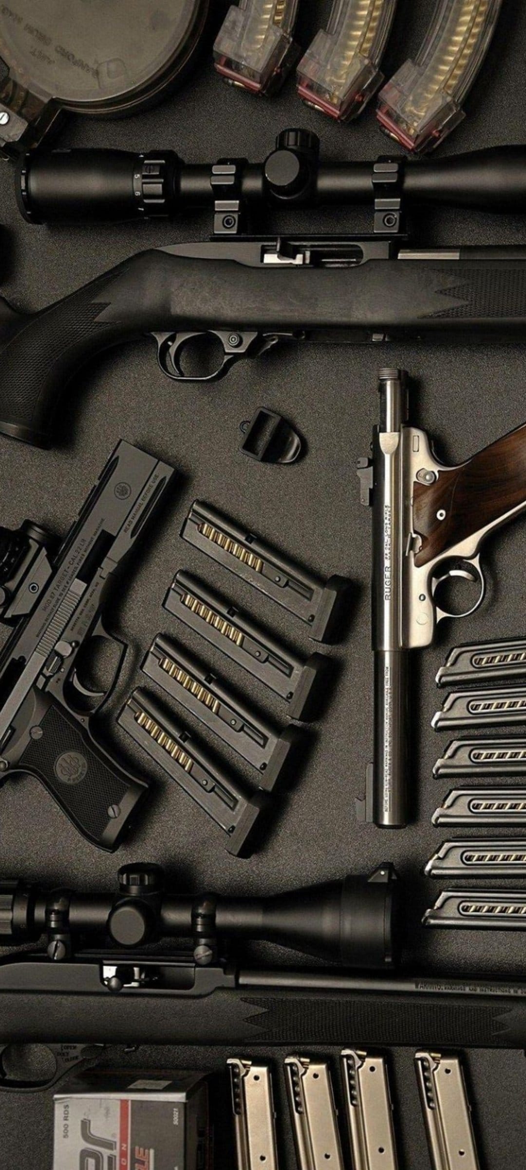 Rifle with a scope and a handgun rest beside brass ammunition cartridges on a dark, textured flat lay surface.