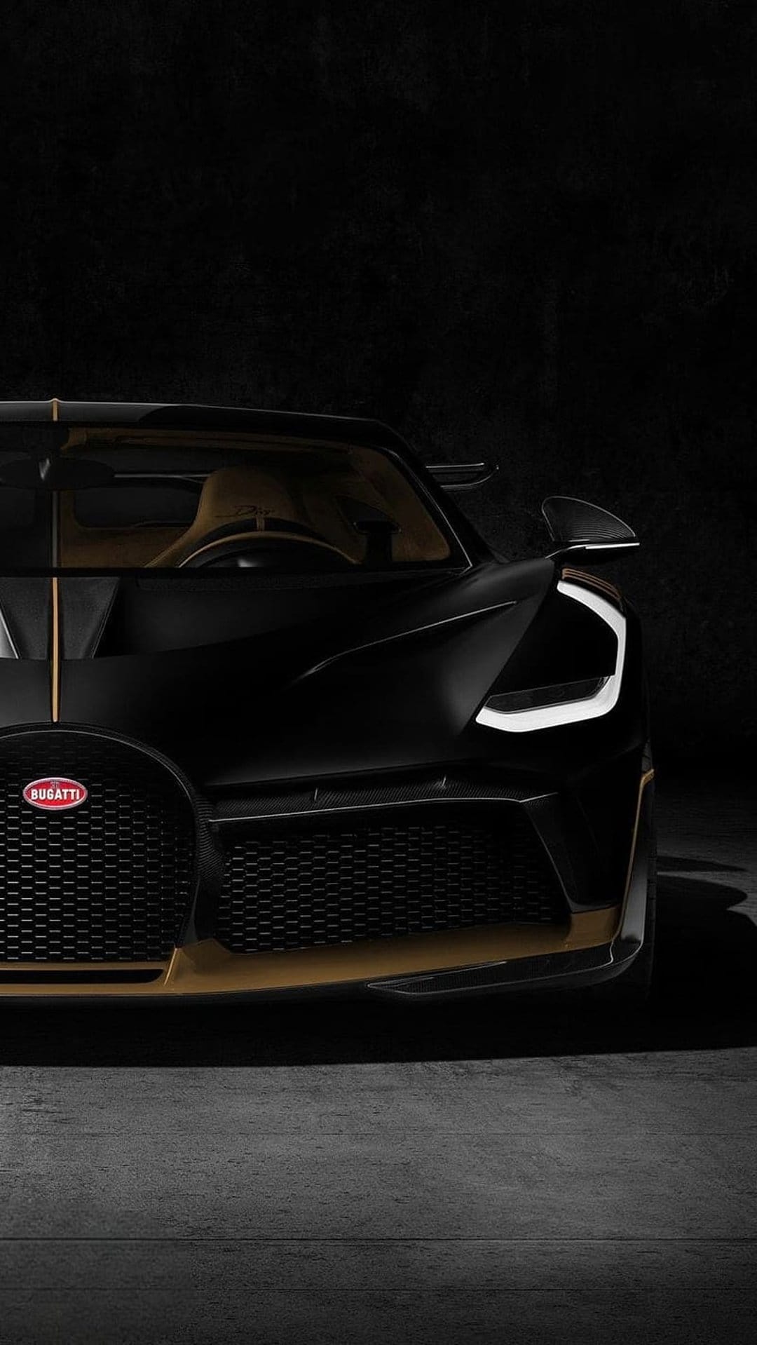Black Bugatti Chiron front grille with gold accents and a C-shaped LED headlight against a dark textured wall.
