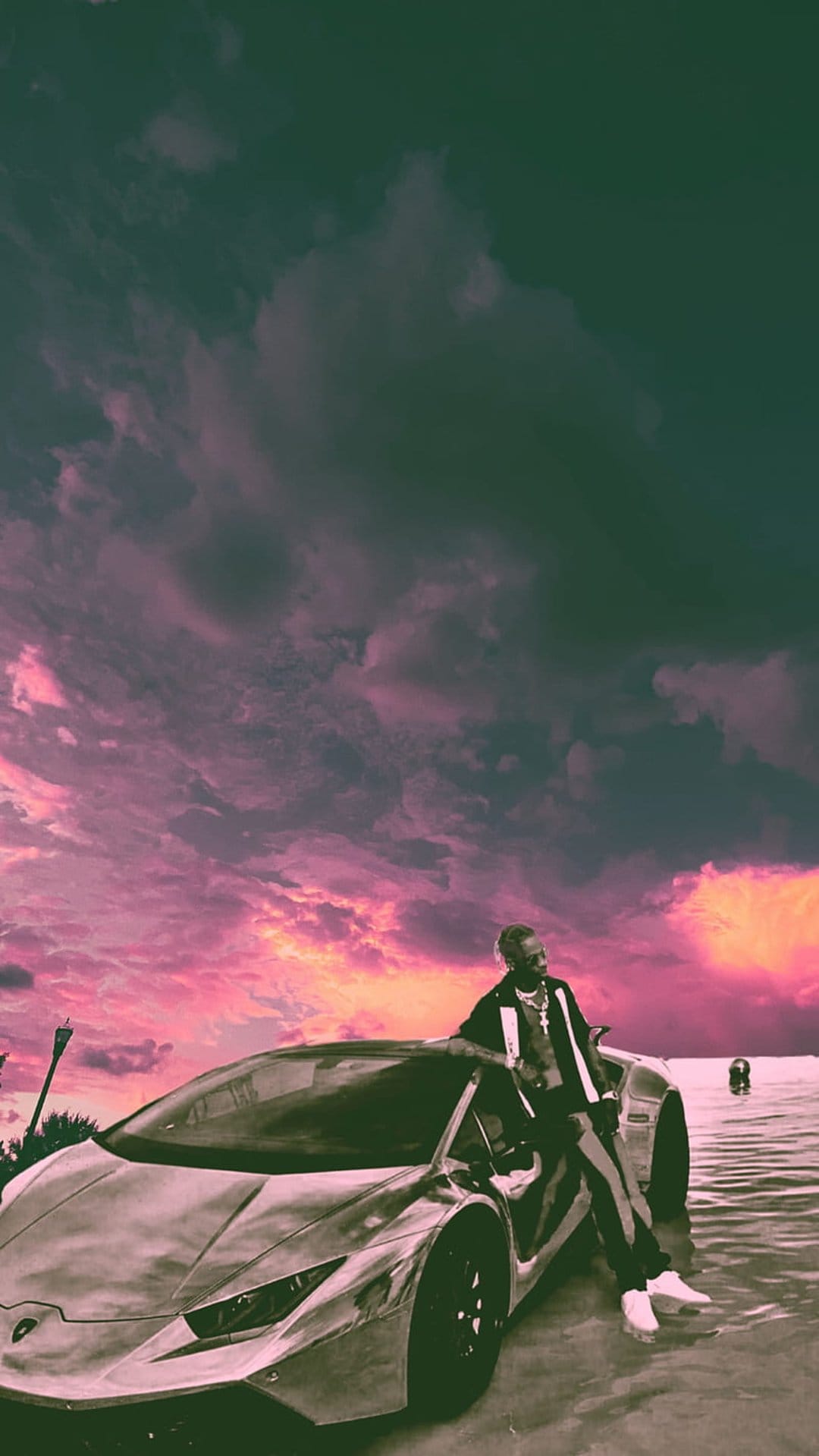 Young Black man in streetwear leans on a silver supercar in shallow water under a pink and purple sunset sky.