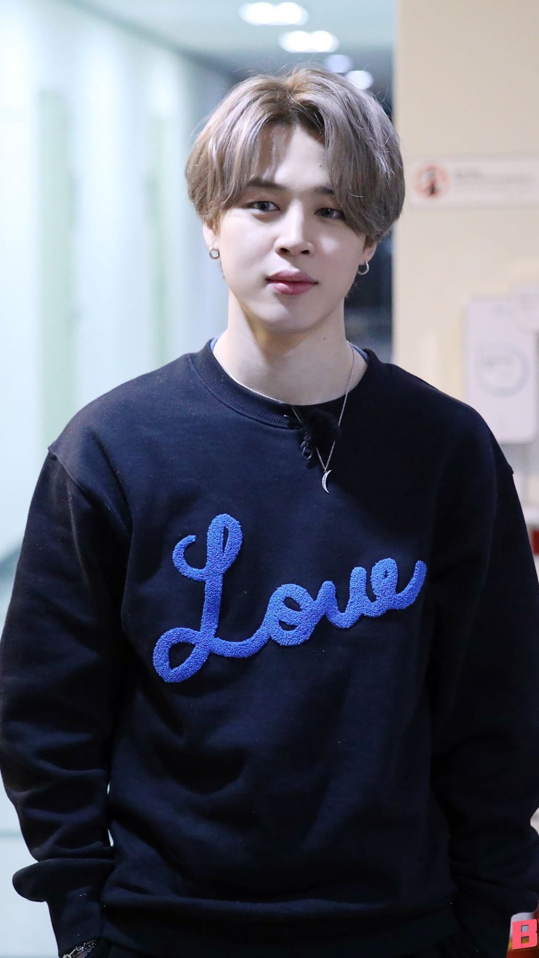BTS member Jimin wearing a black sweatshirt with a blue Love graphic and a crescent moon necklace in a portrait.