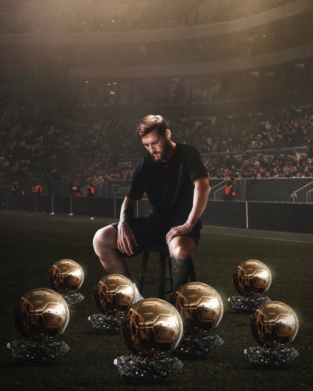Lionel Messi sits on a stool surrounded by various golden trophies on a dark, grass stadium field at night.