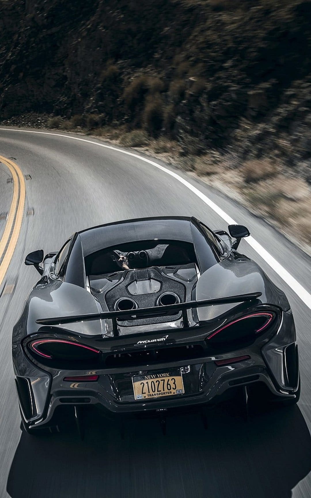 McLaren 570S rear exterior with glowing taillights speeding through a blurred mountain road during daytime.