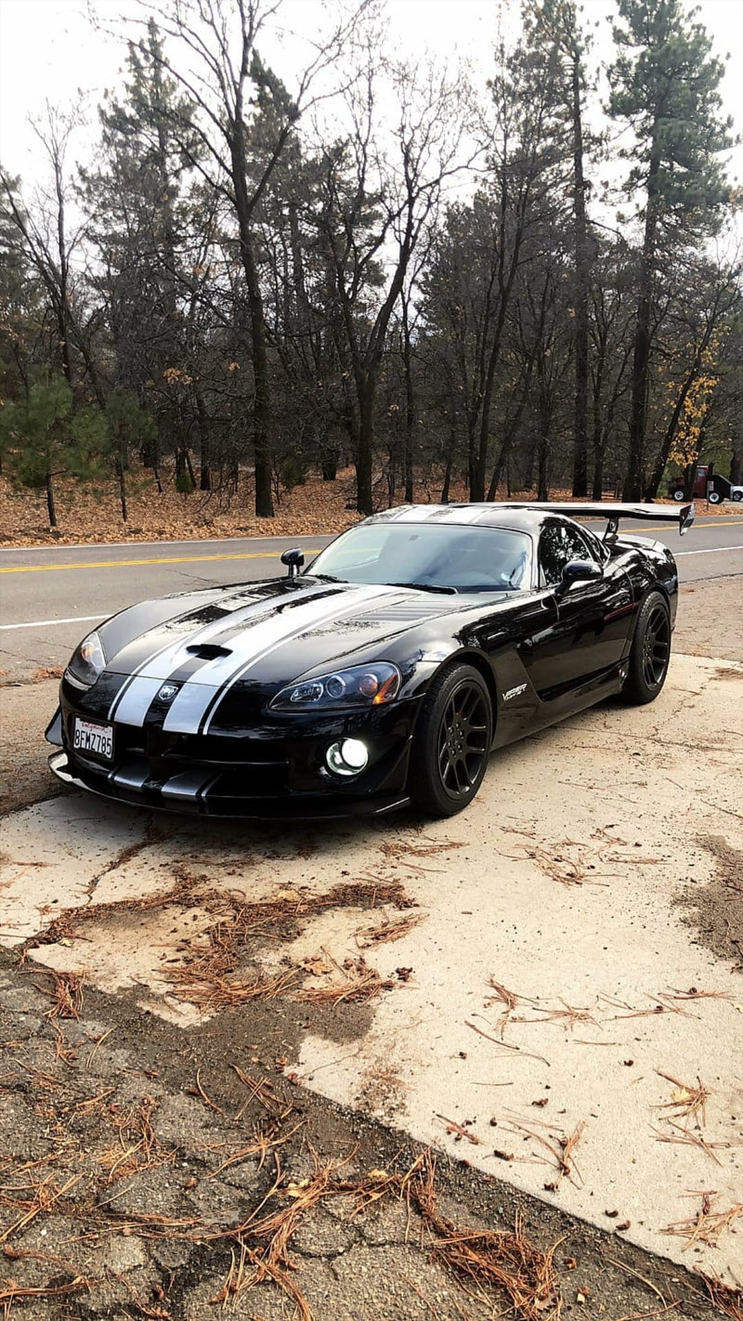 Black Dodge Viper SRT-10 ACR with white stripes and a large rear wing parked on a concrete roadside pad.
