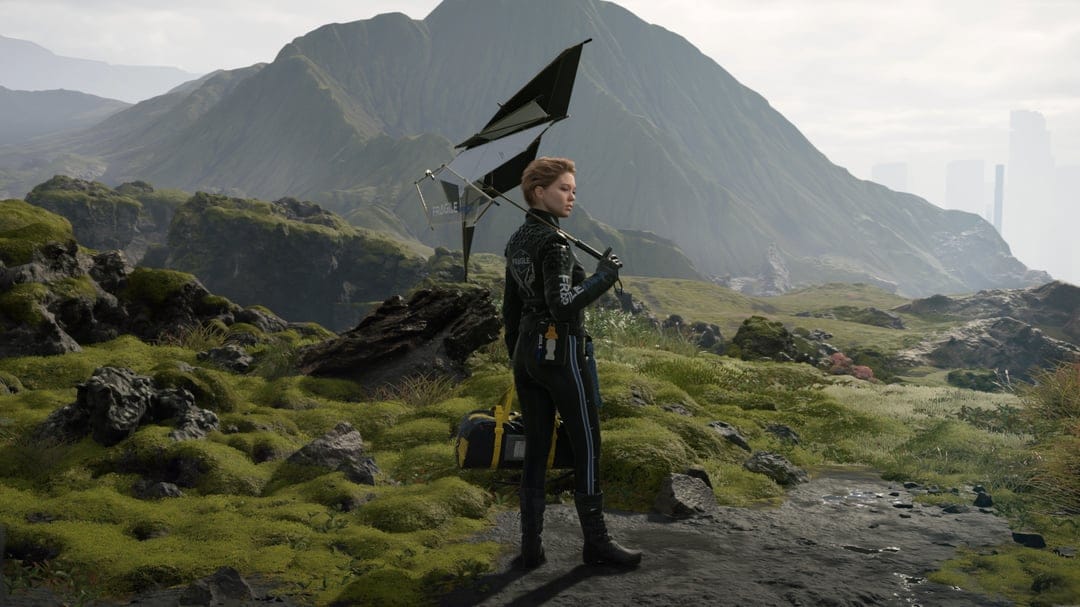 Fragile from Death Stranding holds a black umbrella in a vast green mossy mountain valley under a grey sky.