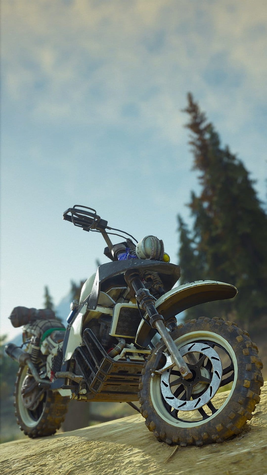 Modified dirt bike with cargo gear parked on a sandy forest incline against a backdrop of hazy pine trees.