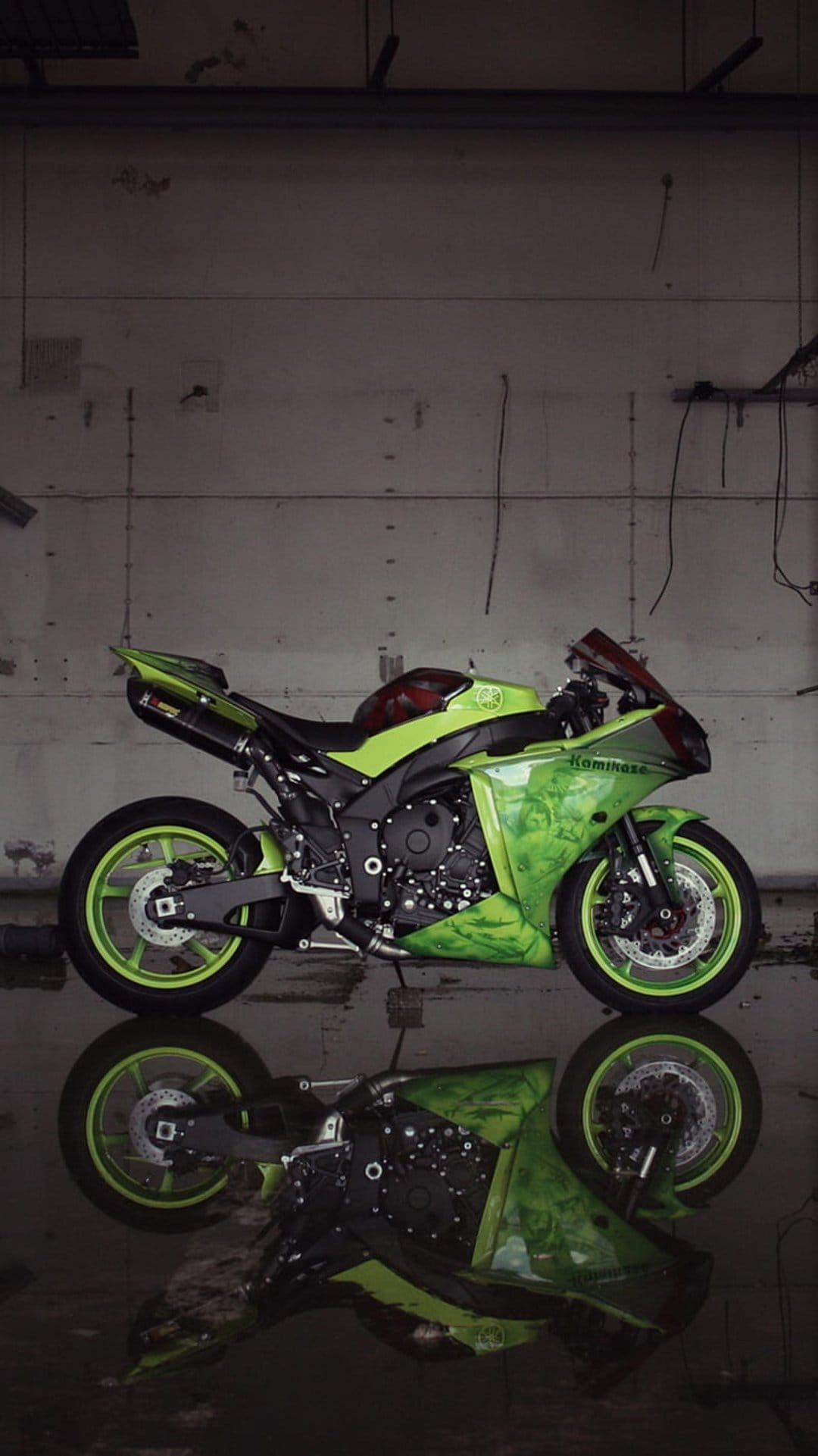 Custom green sportbike with neon accents reflects in a puddle on a dark, wet industrial garage floor.