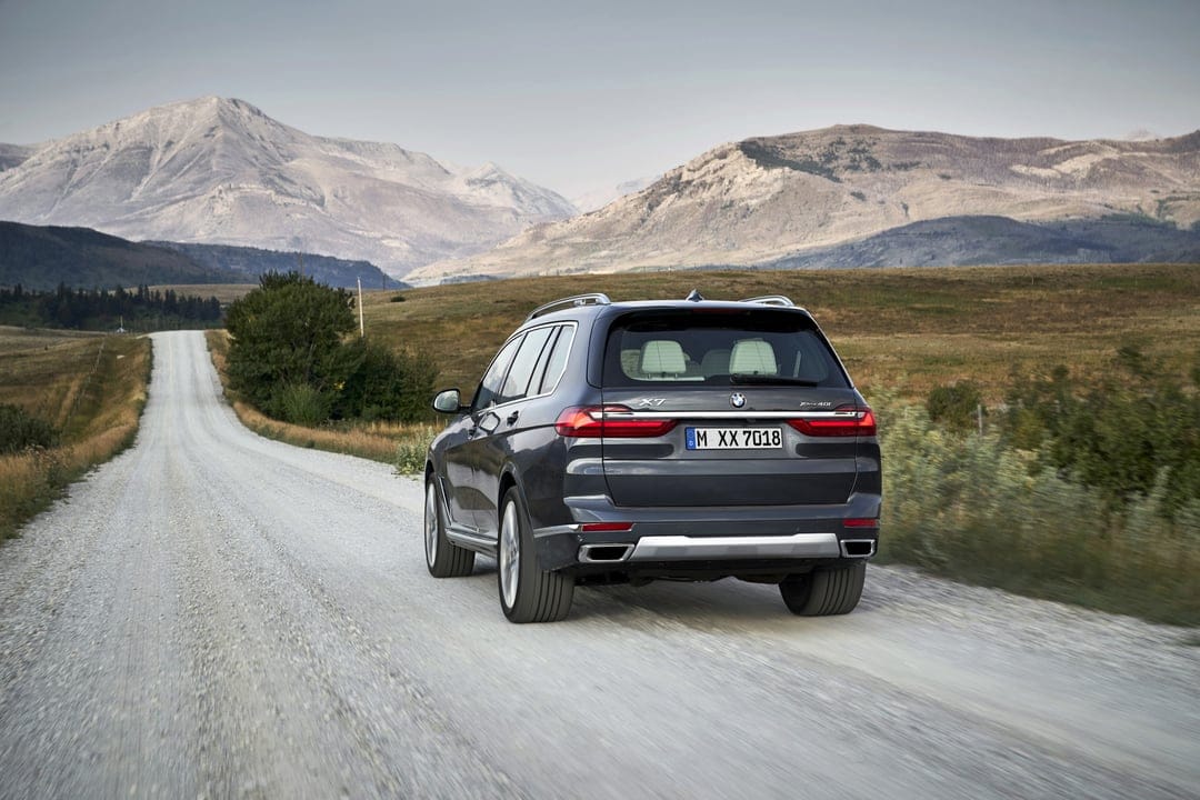 Dark gray BMW X7 SUV driving on a white gravel road with large mountains and hills in the background.