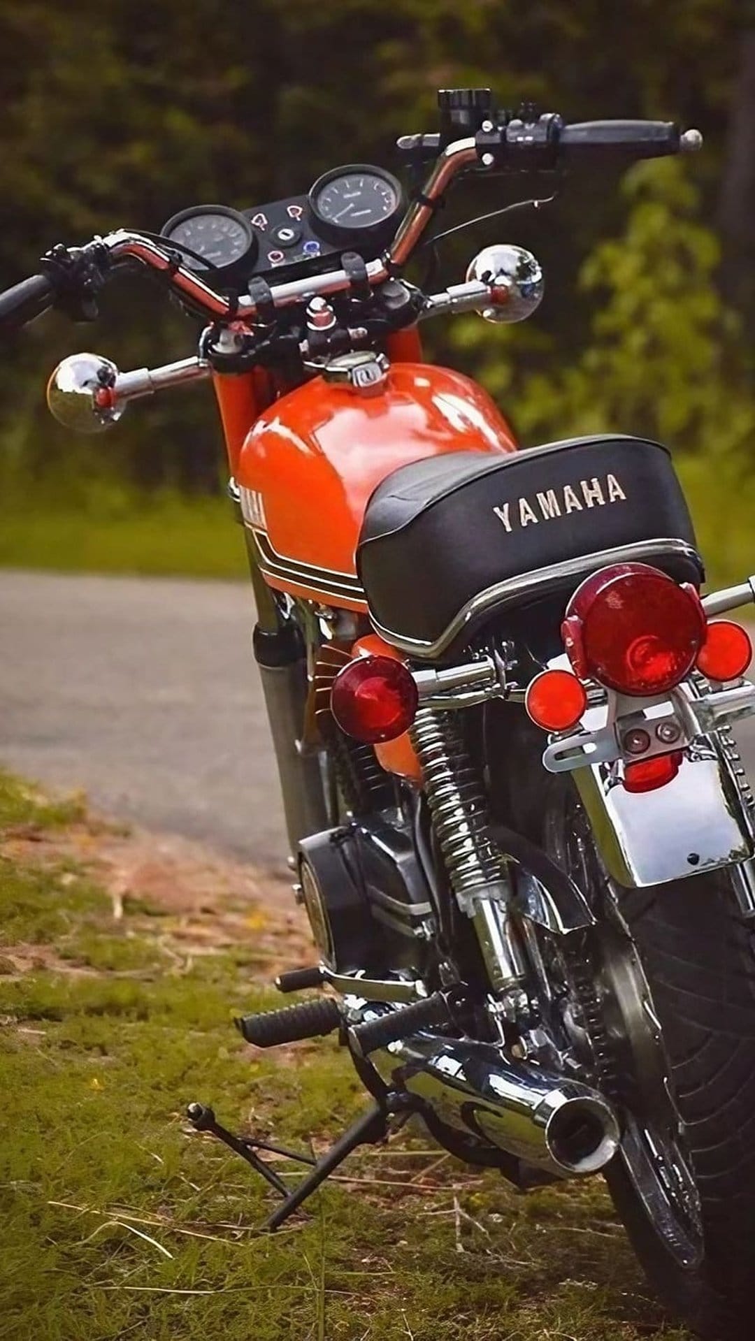 Orange Yamaha motorcycle rear view featuring chrome fenders and red taillights while parked on a grassy field.