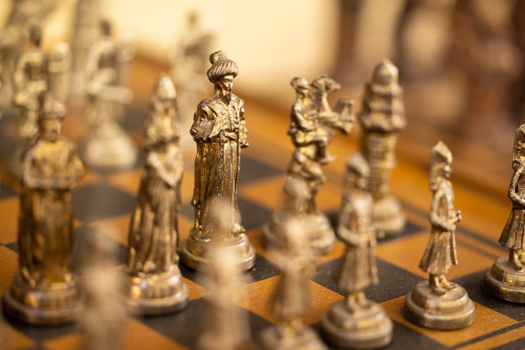 Golden king and queen chess pieces stand on a dark wooden board with warm lighting and shallow depth of field.