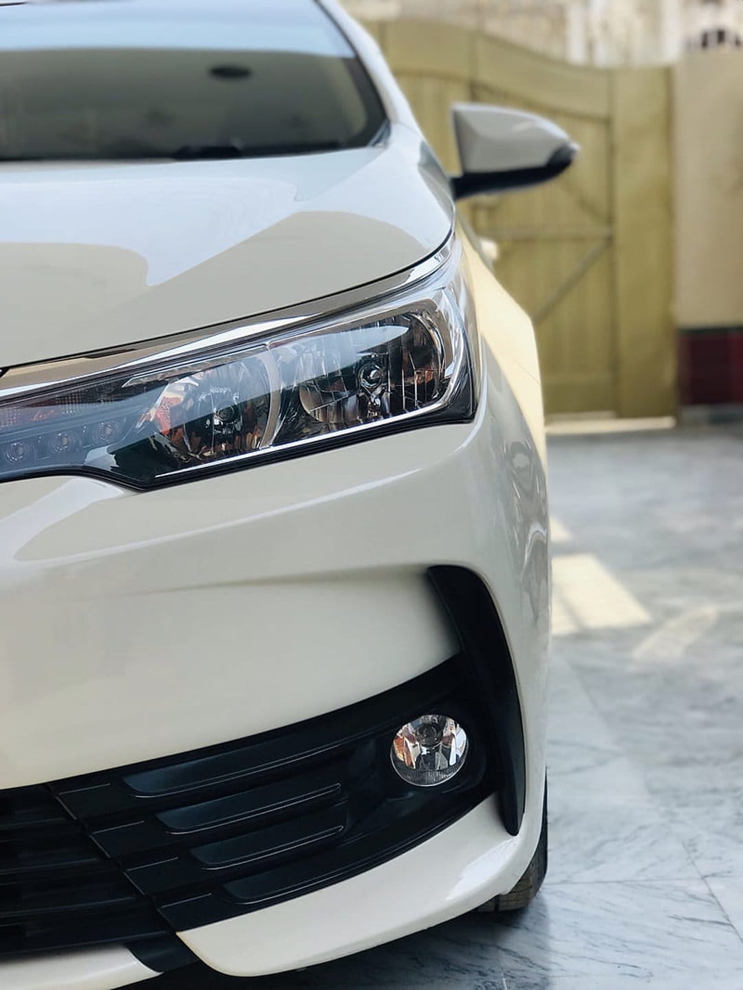White car headlight and black honeycomb grille showing intricate internal glass housing and polished paint.