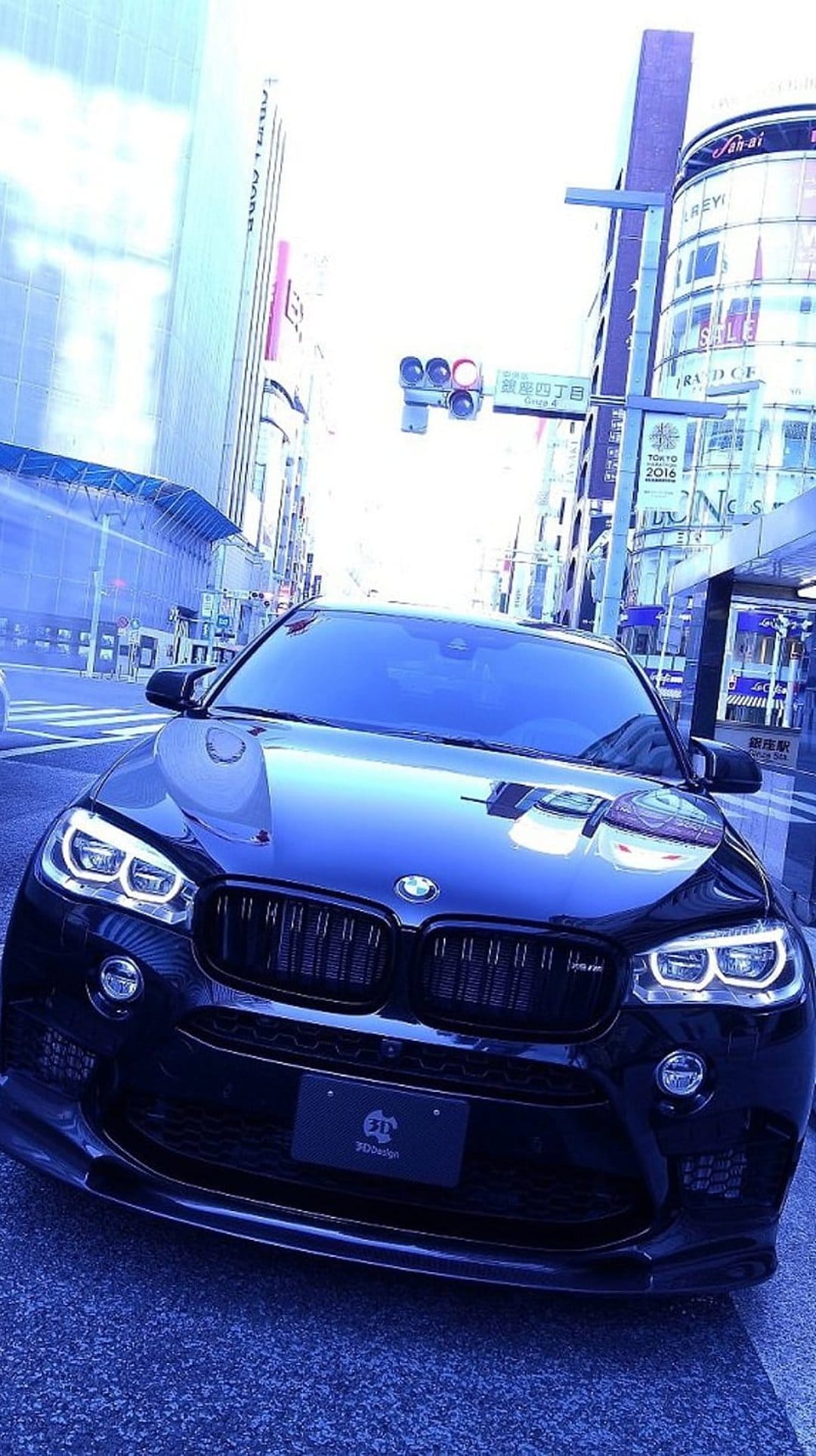 Black BMW SUV with glowing headlights on a Tokyo city street at night beneath illuminated skyscrapers and signs.
