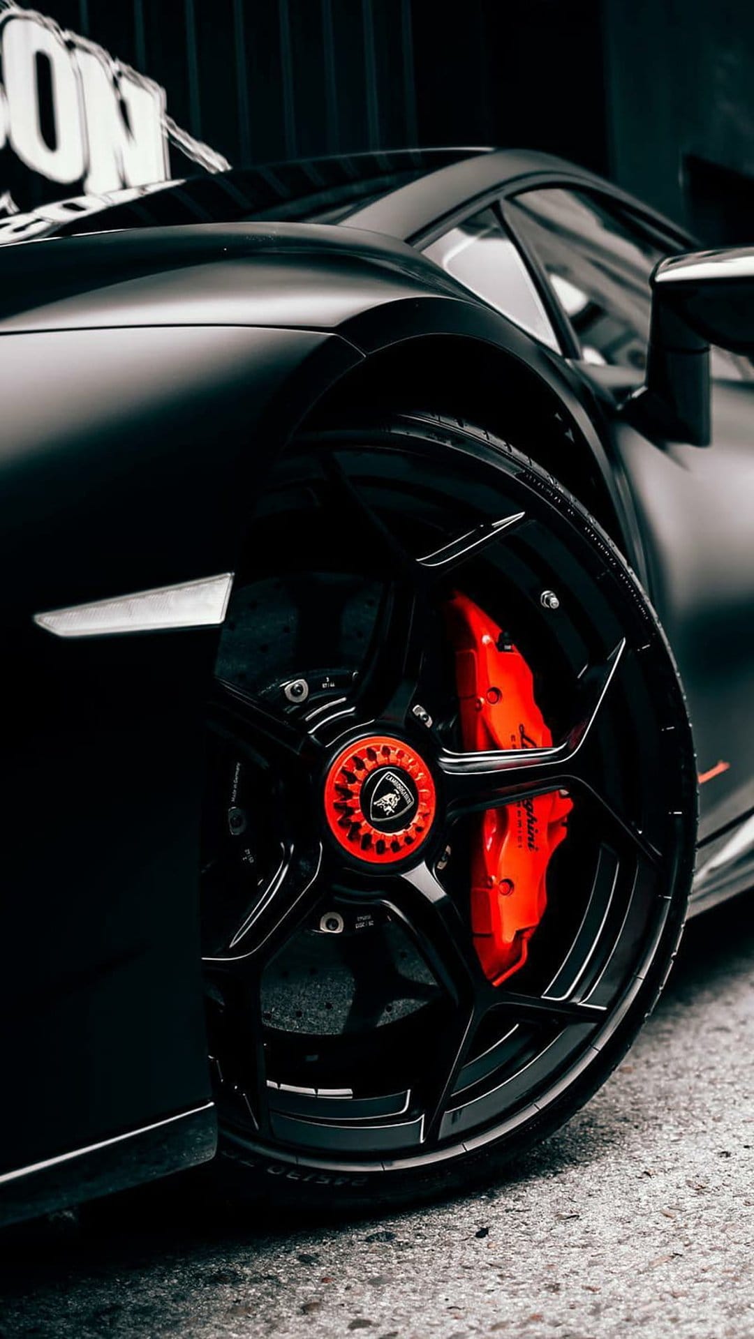 Lamborghini matte black wheel rim with vibrant red brake calipers and a detailed center locking hub assembly.