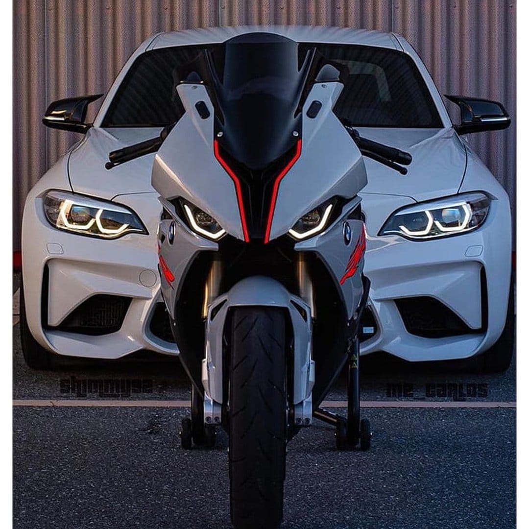 White BMW M2 car and sportbike motorcycle with red accents parked side-by-side against a grey textured wall.