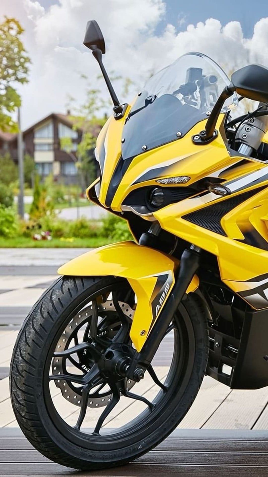 Yellow sportbike front wheel and aerodynamic fairing with a blurred suburban background during daylight.