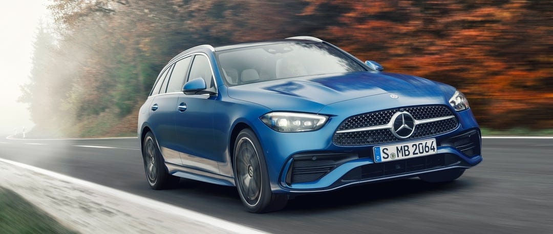 Blue Mercedes-Benz wagon driving past orange autumn trees on a misty forest road with motion blur.