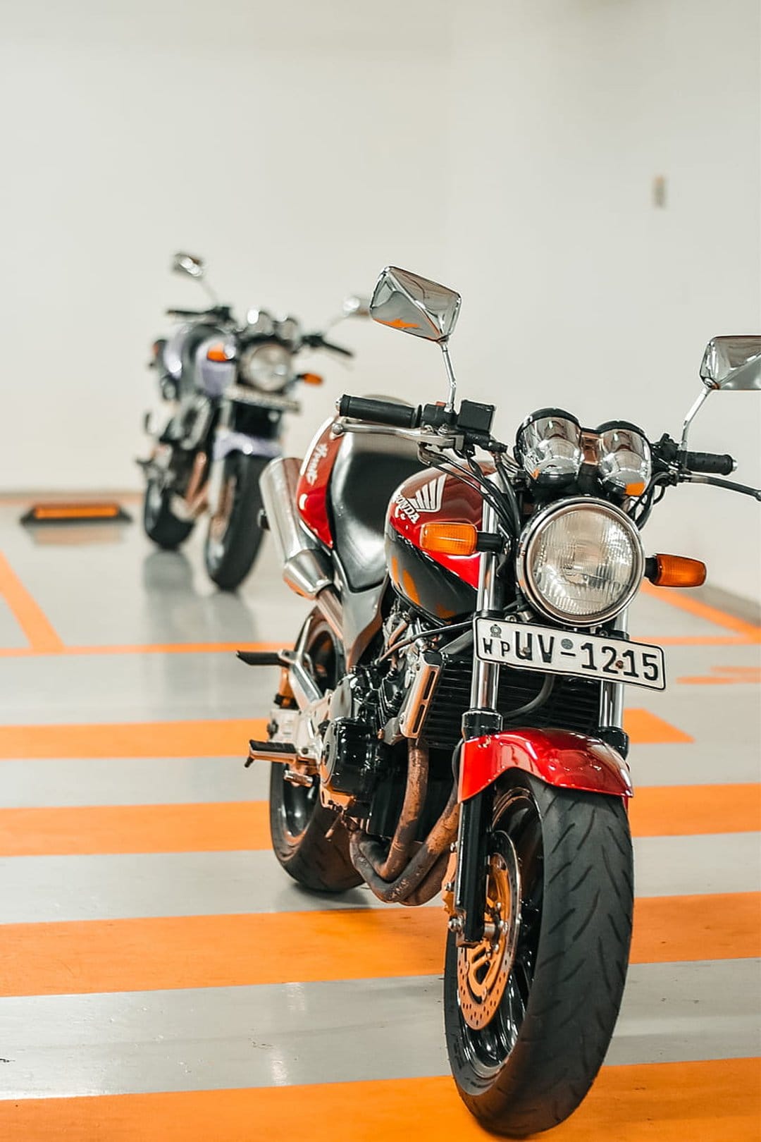 Red sportbike on orange-striped garage flooring with a purple motorcycle blurred in the background.