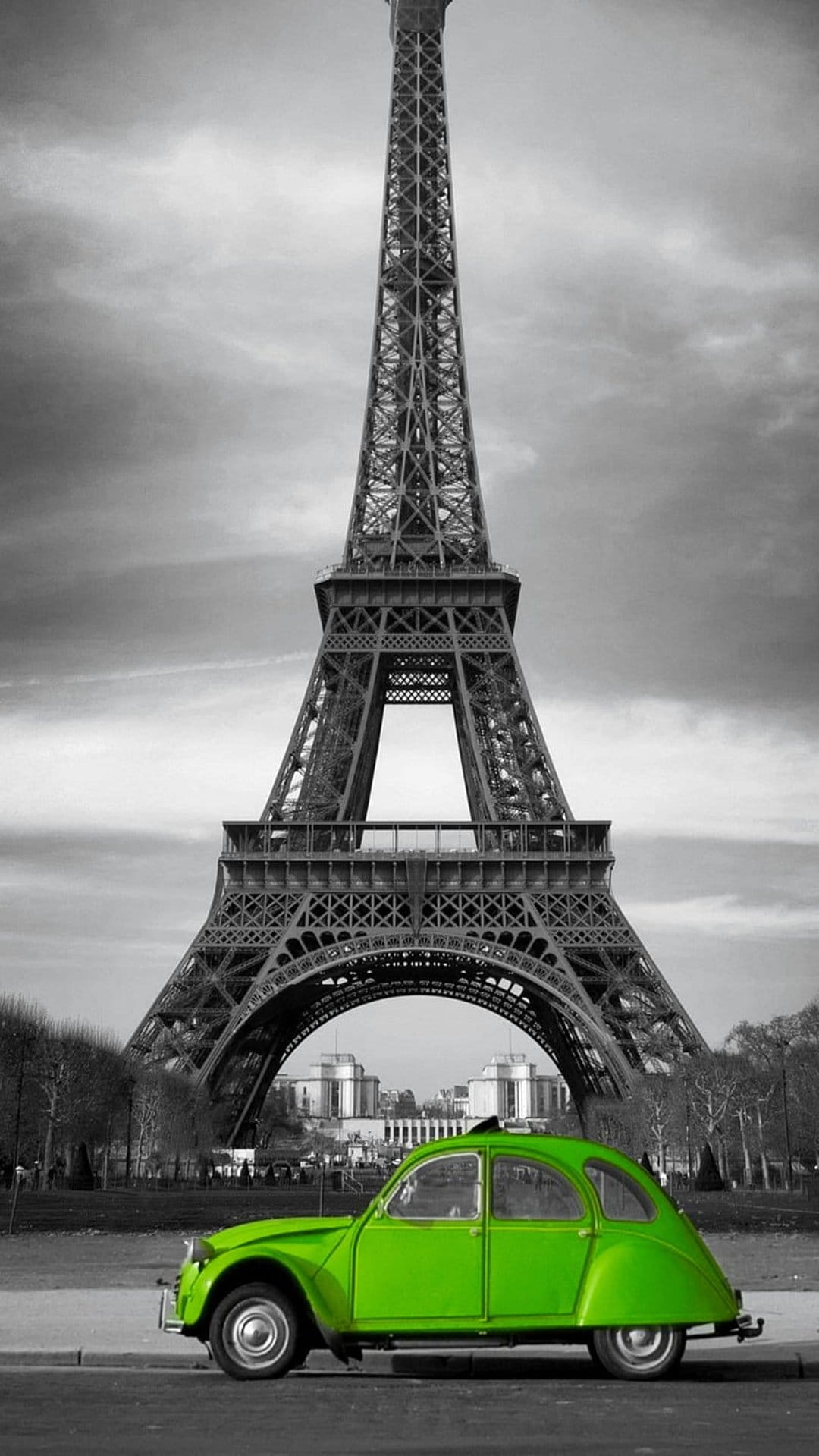 Bright green vintage car parked in front of the black and white Eiffel Tower under a cloudy Parisian sky.