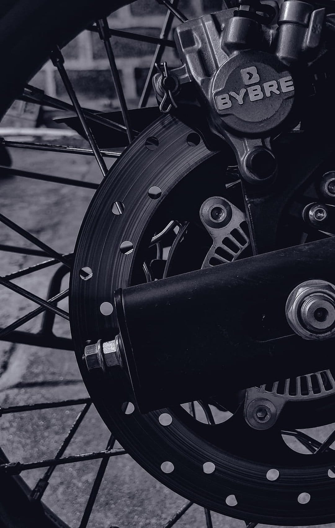 Rear brake disc and BYBRE caliper in monochrome showing drilled metal textures and rugged mechanical bike parts.