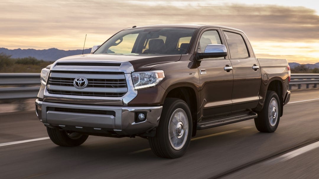 Brown Toyota Tundra 1794 Edition driving on a desert highway with mountains under a vibrant sunset sky.