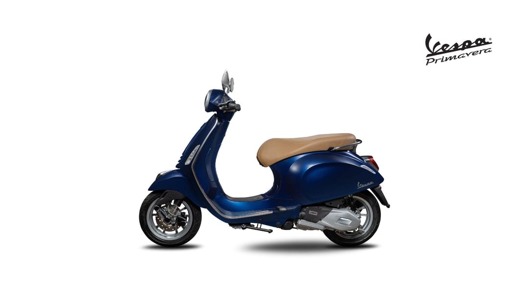 Blue Vespa Primavera scooter with a tan seat in a side profile view against a clean white studio background.